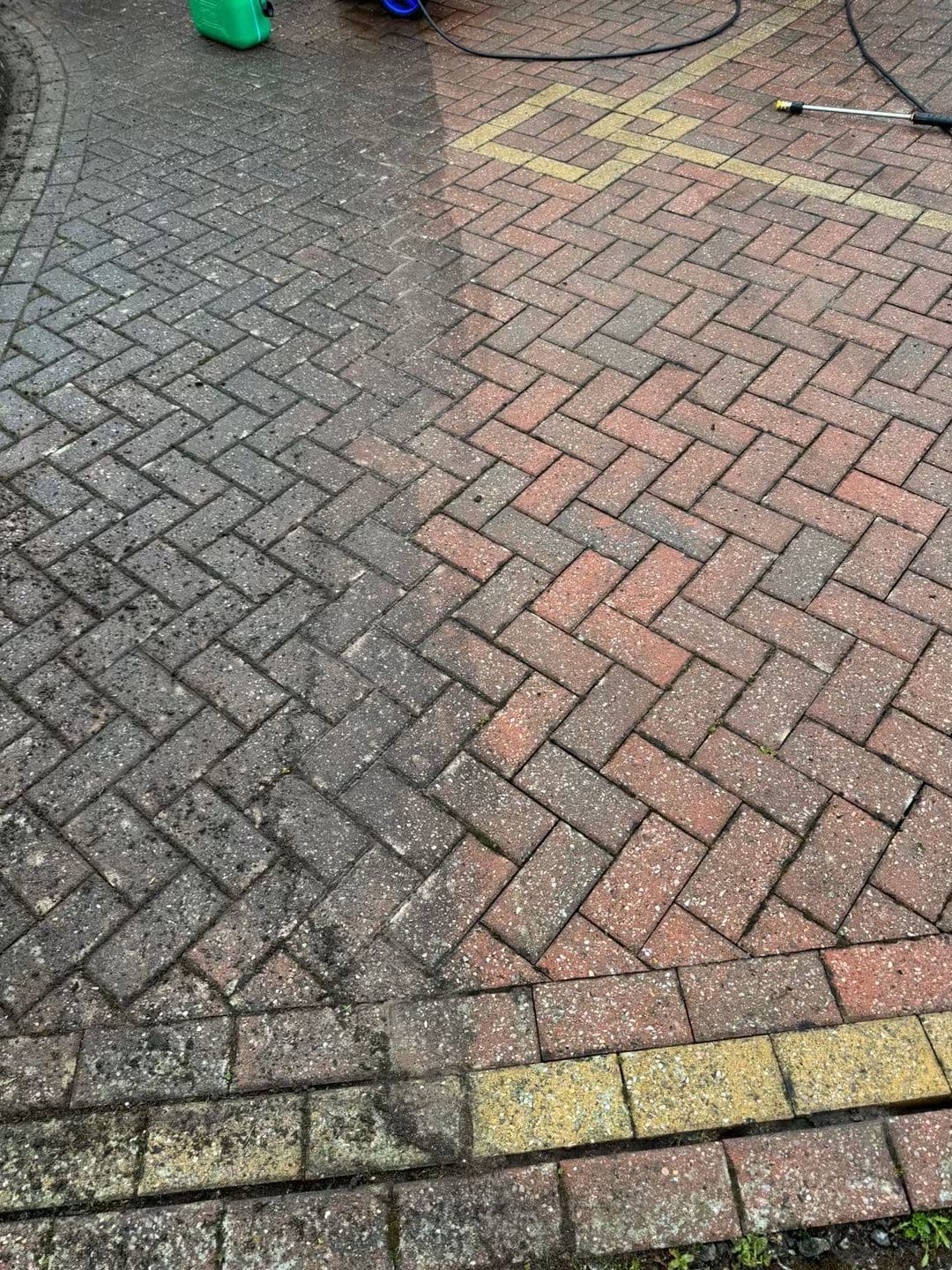 Red block paving driveway with the left half dull and weathered and the right half pressure washed to a brighter red, with the pressure washer lance beside it