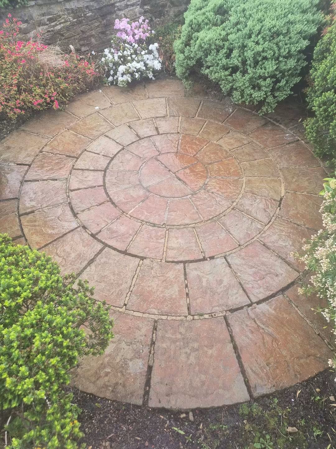Circular sandstone patio after pressure washing, a cleaner terracotta colour with shrubs and flowers around it